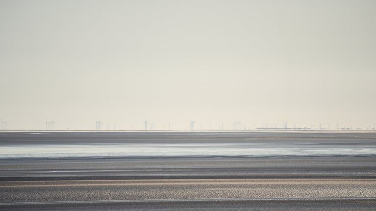 View across the estuary at low tide. There are wind turbines in the distance.